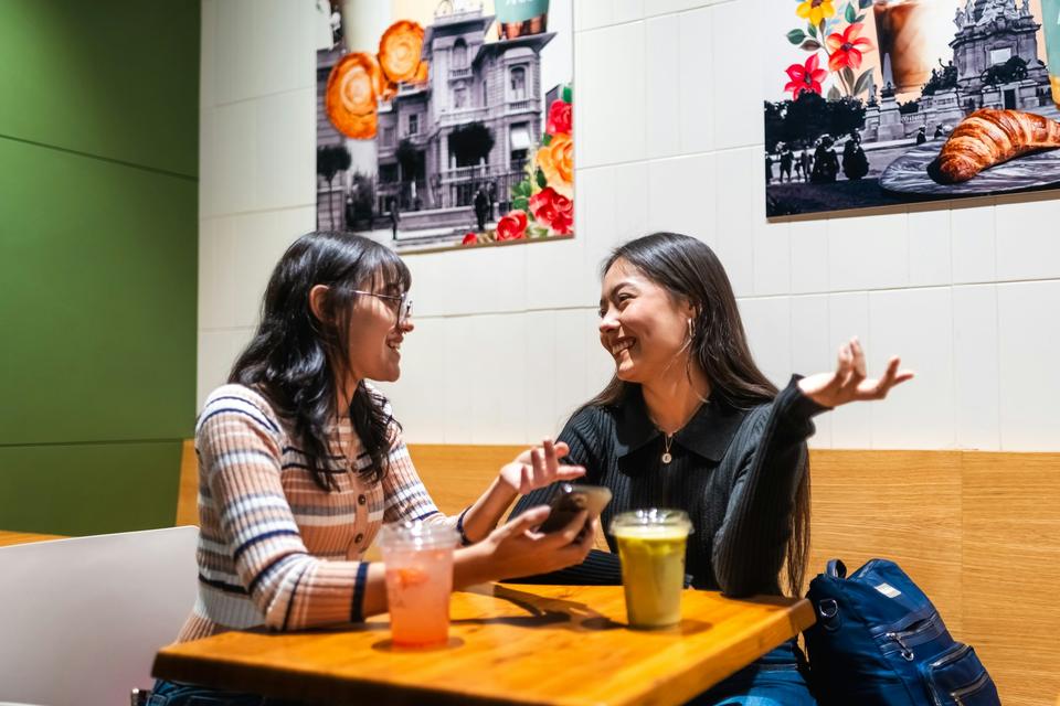 Two friends talk at a café table.