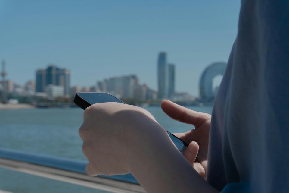 Hands holding a phone by the water.