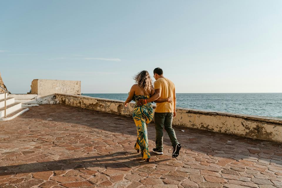 A couple walks across a seaside terrace.