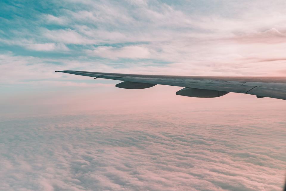An airplane wing above pink clouds.